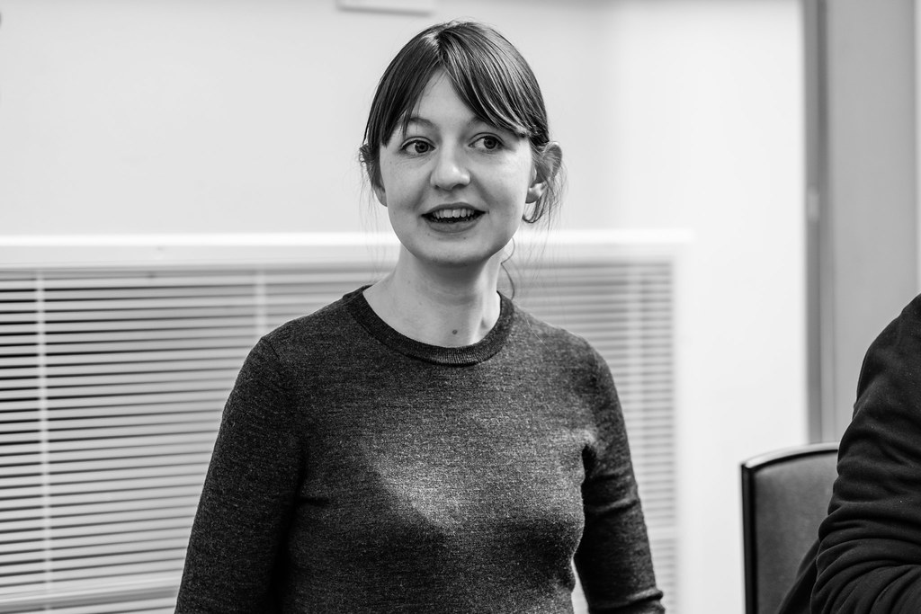 A black-and-white photo of Sally Rooney. The author, dressed casually in a sweater, appears to be looking at something off to the side of the camera.