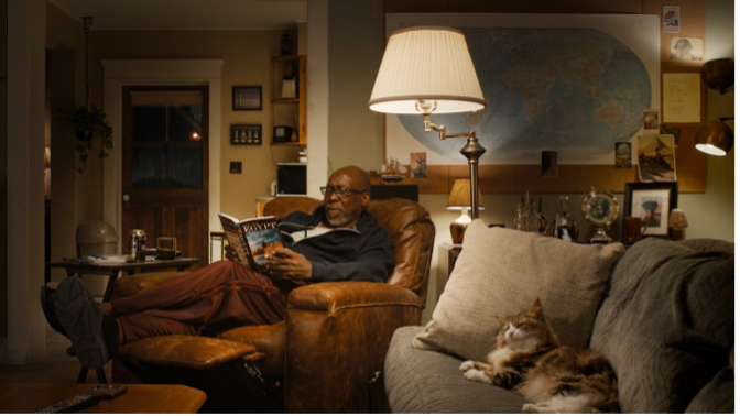 Ernie reclining in an armchair reading a book about Egypt in a living room with a cat to his right.