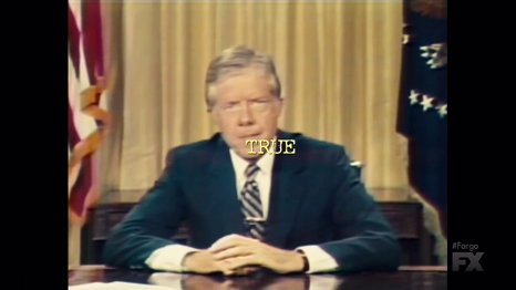 Jimmy Carter sits at a desk in a blue suit. Flags and a yellow curtain are behind him. Yellow text superimposed on his face reads: 