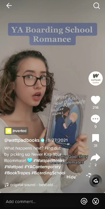 Screenshot from a tiktok video from the @wattpadbooks account on 9/27/21. Image shows a young person holding a book titled Never Kiss Your Roommate by Philline Harms. First caption reads: "YA Boarding School Romance." Main caption reads: "What happens next? Find out by picking up Never Kiss Your Roommate!"