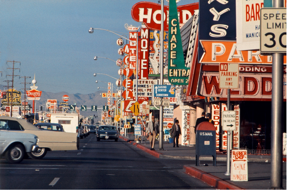 A 1960s Las Vegas streetscape, crowded with signage