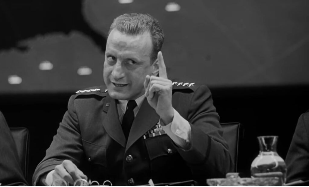 [Alt-Text: The actor George C. Scott as General Buck Turgidson, looking serious with one finger raised as he makes his point.]