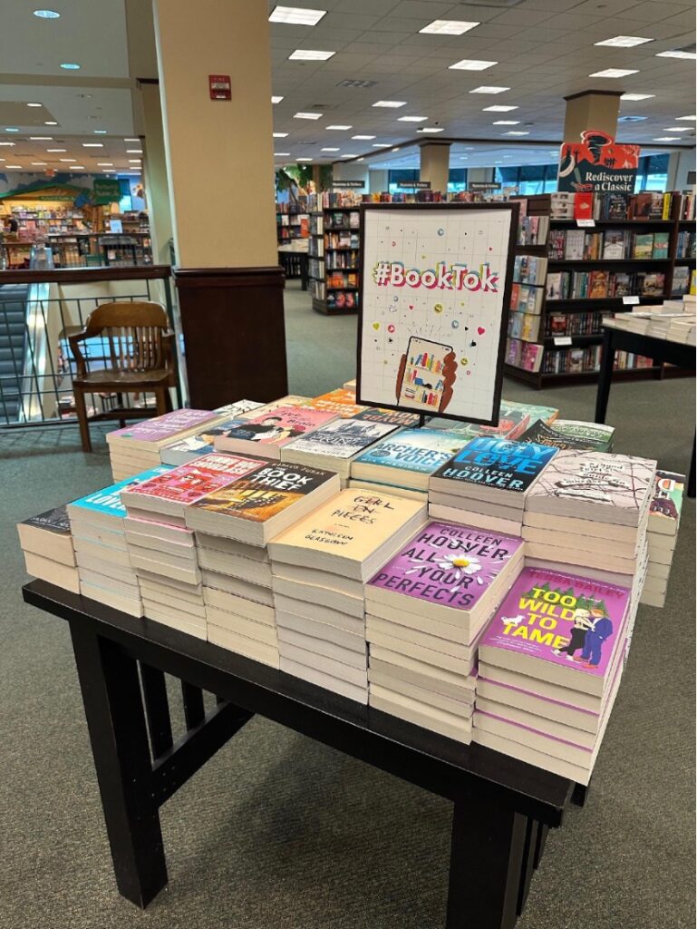 A table covered in stacks of books and featuring a sign that reads 